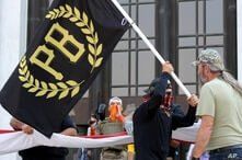 A protester carries a Proud Boys banner, a right-wing group, while other members start to unfurl a large U.S. flag in front of…