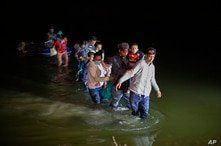 Migrant families, mostly from Central American countries, wade through shallow waters after being delivered by smugglers on small inflatable rafts on U.S. soil in Roma, Texas, March 24, 2021.