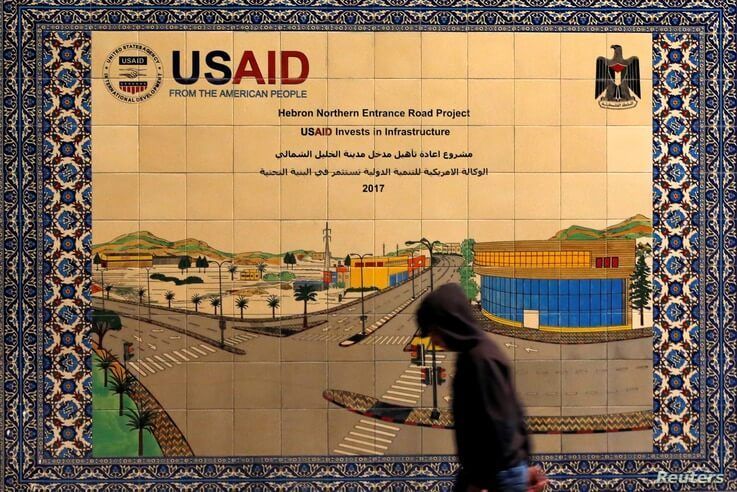 A Palestinian walks past a ceramic sign of a U.S. Agency for International Development (USAID) project in Hebron in the Israeli…