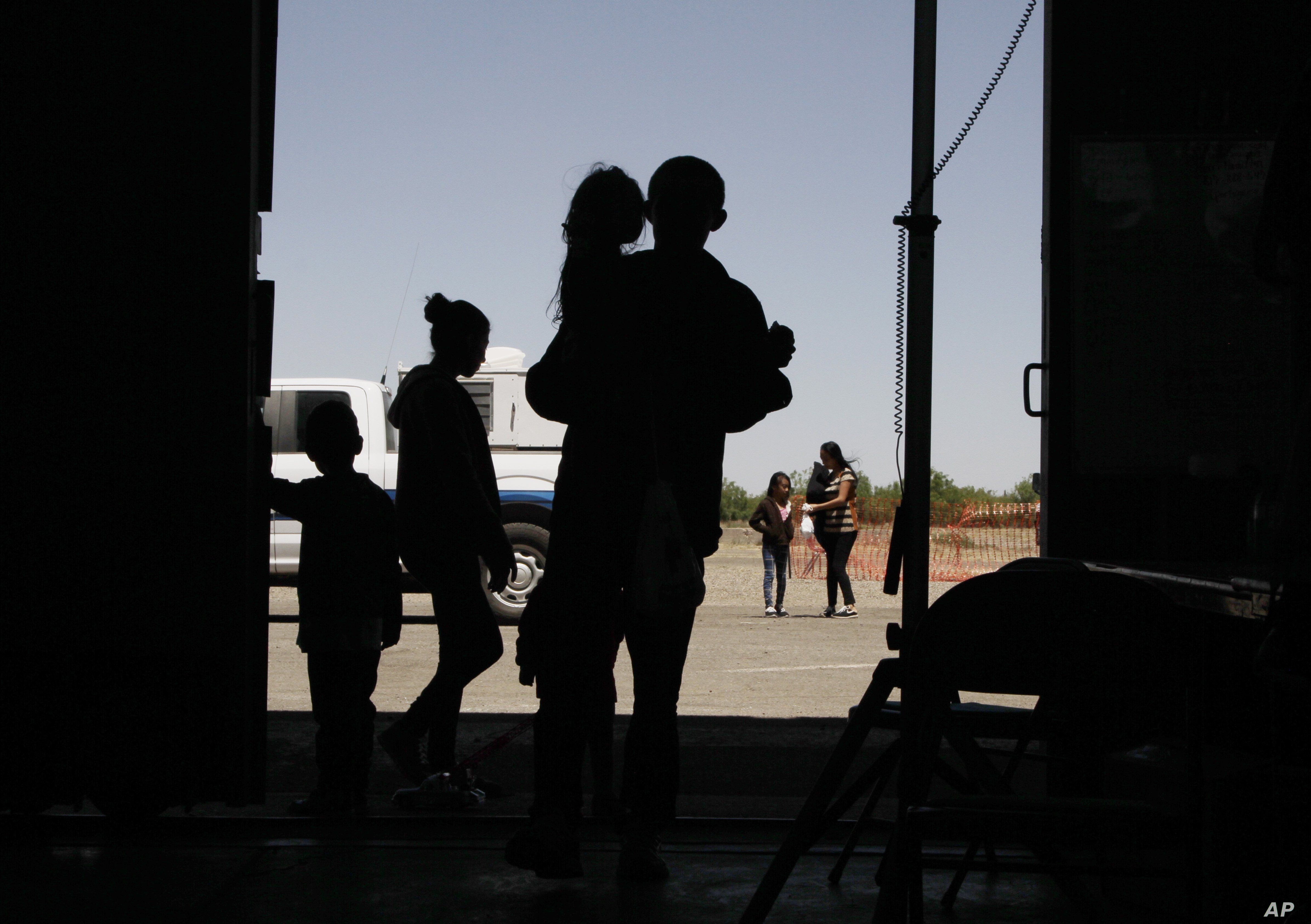 FILE - Migrants, mainly from Central America, guide their children into a World War II-era bomber hanger in Deming, N.M. A panel of appeals court judges in California will hear arguments over conditions in detention and holding facilities near the border.