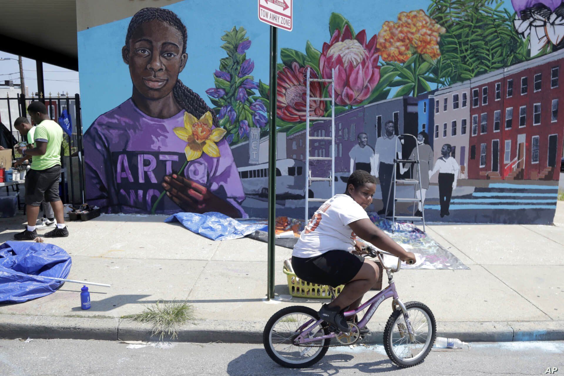 A boy rides his bicycle, July 29. 2019, after volunteering to paint a mural outside the New Song Community Church in the Sandtown section of Baltimore. 