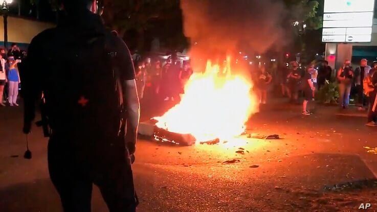 In this image taken from video a mattress burns in the street near the Portland Police Bureau's North Precinct Sunday night,…