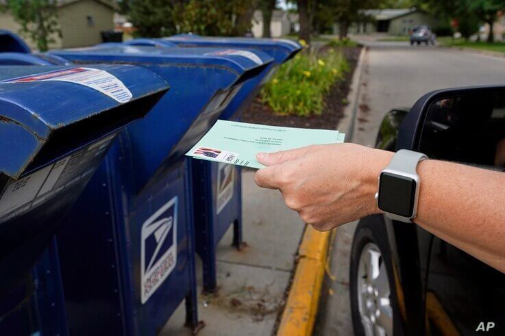 FILE - In this Tuesday, Aug. 18, 2020, file photo, a person drops applications for mail-in-ballots into a mail box in Omaha,…