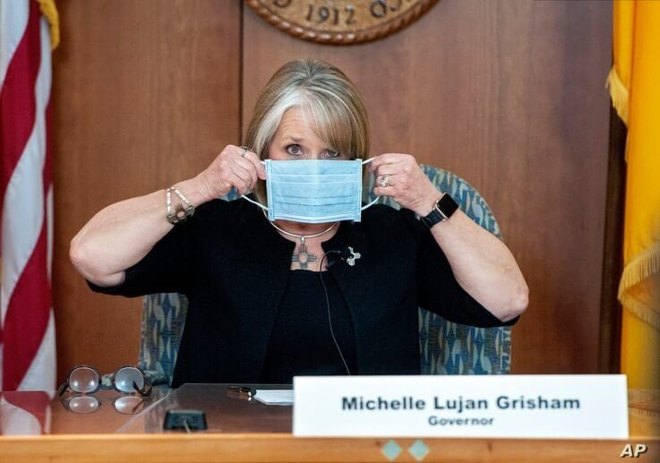 FILE - In this April 15, 2020, file photo, New Mexico Gov. Michelle Lujan Grisham puts on her face mask when not speaking…