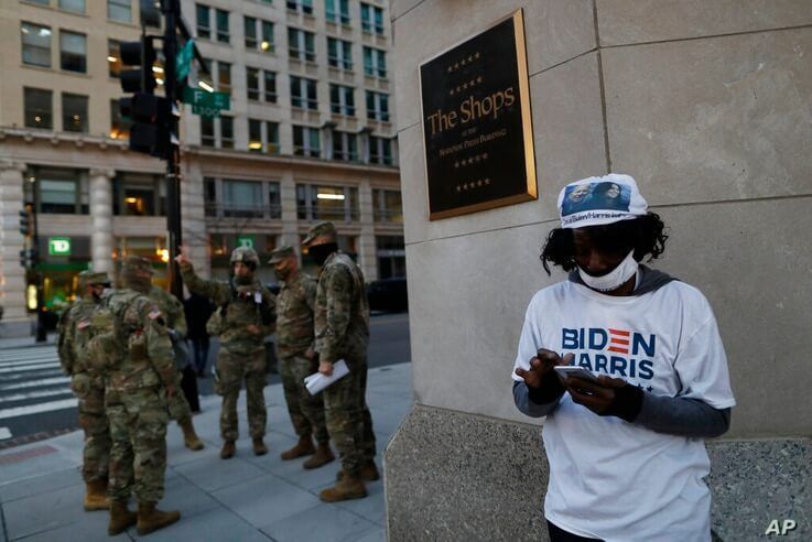 A Biden-Harris supporter stands at a corner as National Guards deploy around the city ahead of President-elect Joe Biden's…