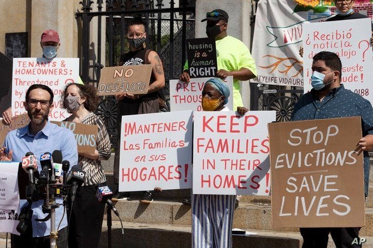 People from a coalition of housing justice groups hold signs protesting evictions during a news conference outside the…