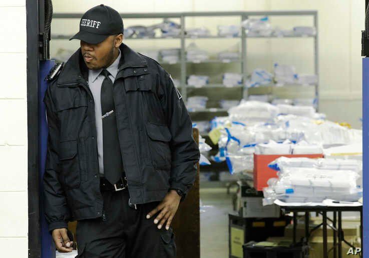 A Milwaukee County sheriff guards a room where ballots are stacked up as a statewide presidential election recount begins…