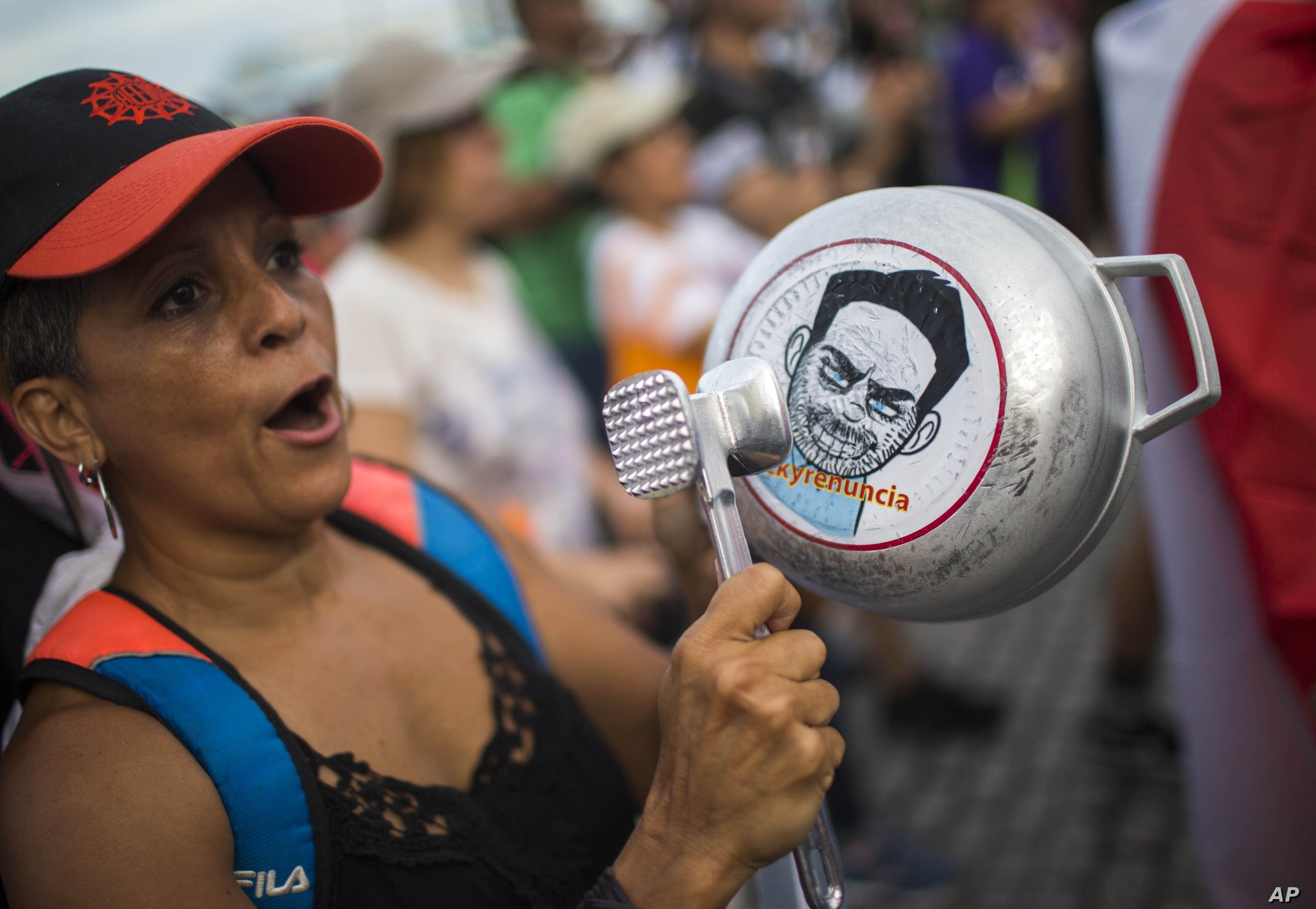 FILE - A demonstrator bangs on a pot that has a cartoon drawing of Governor Ricardo Rossello and text the reads in Spanish 