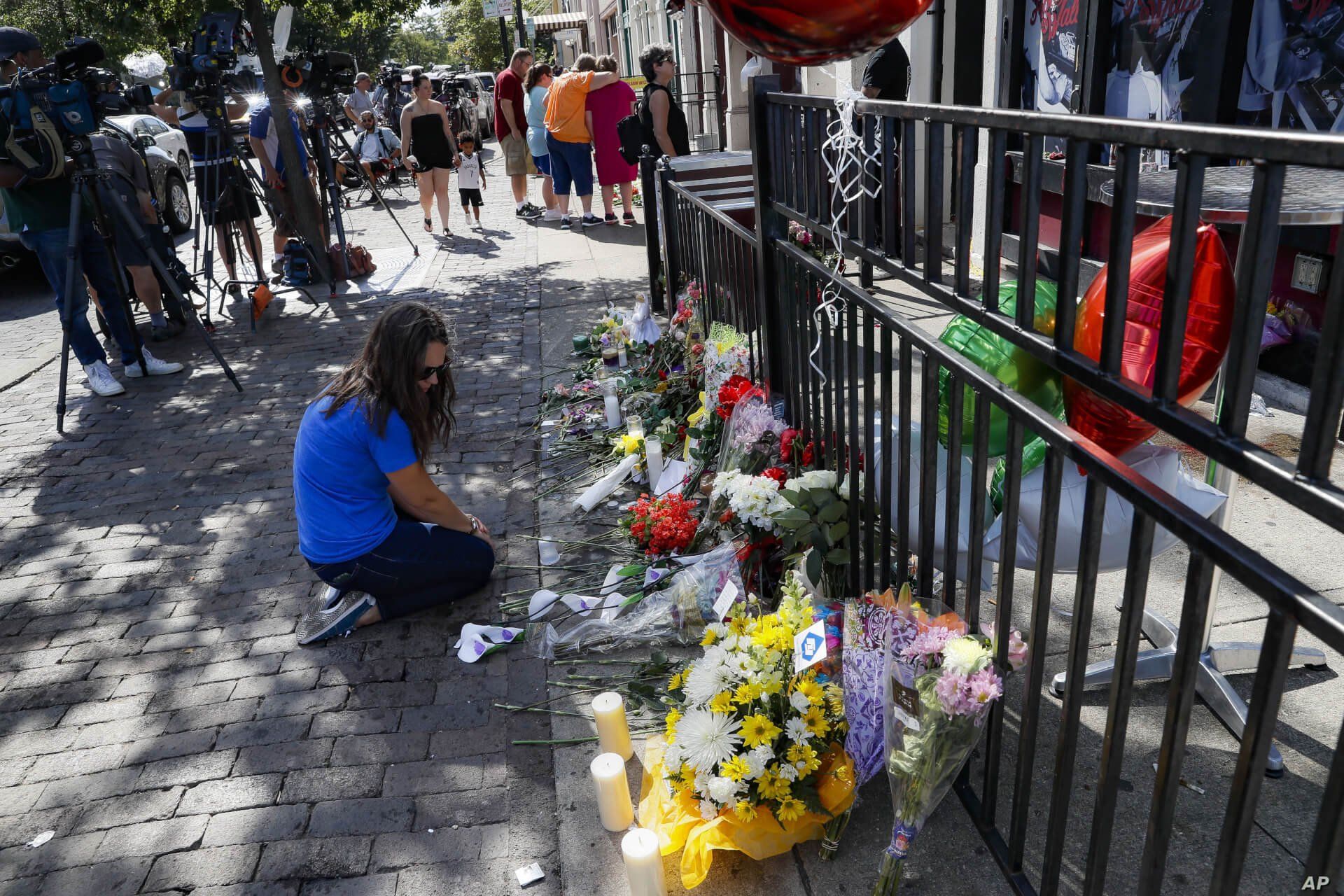 A mourner kneels at a makeshift memorial near members of the media outside the Hole in the Wall bar in the Oregon District in Dayton, Ohio, Aug. 5, 2019.