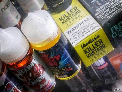 FILE- In this Sept. 16, 2019 file photo Flavored vaping solutions are shown in a window display at a vape and smoke shop in New…