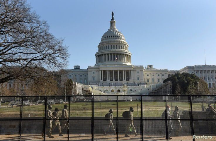 National Guard members walk behind a fence installed in front of the U.S. Capitol, a day after supporters of U.S. President…
