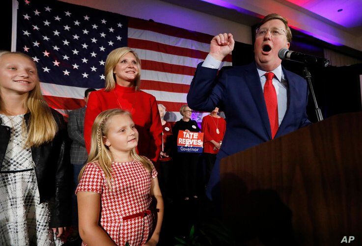 Republican Gov.-elect Tate Reeves addresses his supporters at a state GOP election night event, as wife, Elee Reeves, rear, and…
